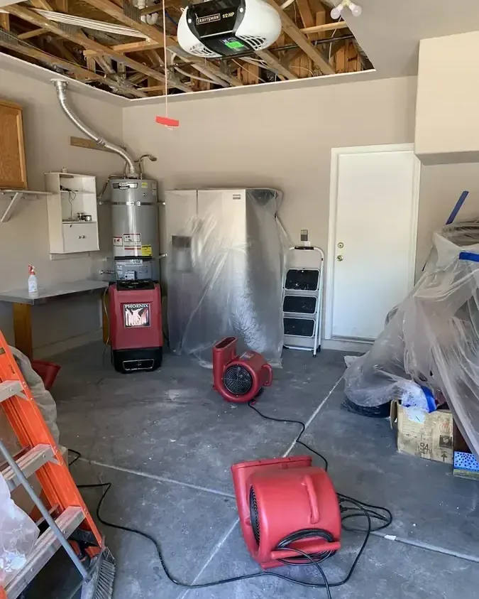 Air movers and a dehumidifier drying a garage after a water heater leak