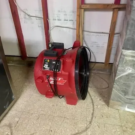 A drying setup for Covington water damage: an air mover, an opened lower wall and hung plastic sheeting.